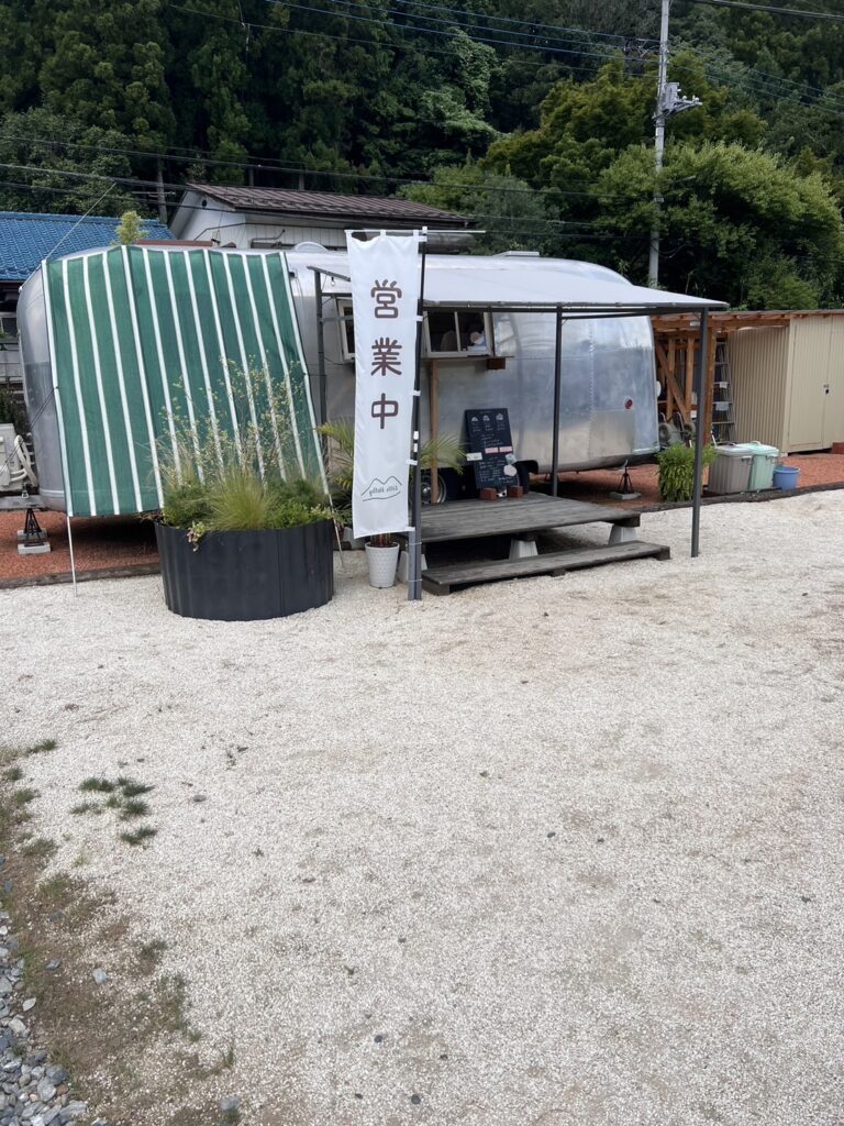 Little Valleyの外観。エアストリーム車体が店舗として使われており、緑のストライプのサンシェードが設置されている。背景には緑豊かな山々が広がっている。