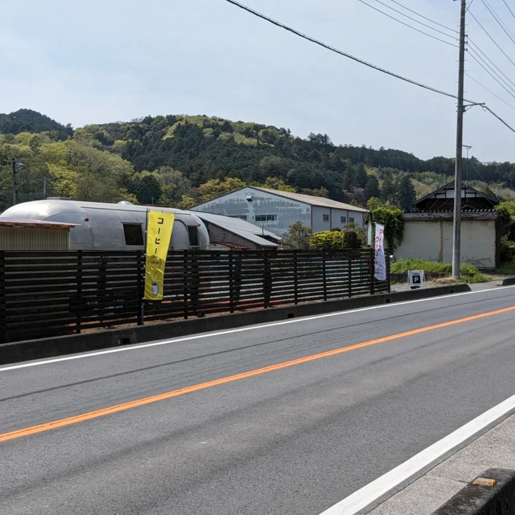 埼玉県日高市にあるアイスクリームショップ『Little Valley』の外観。国道299号線沿いに位置し、エアストリーム車体が特徴的。青空の下、道路沿いに「コーヒー」の黄色いのぼりが目立つ。