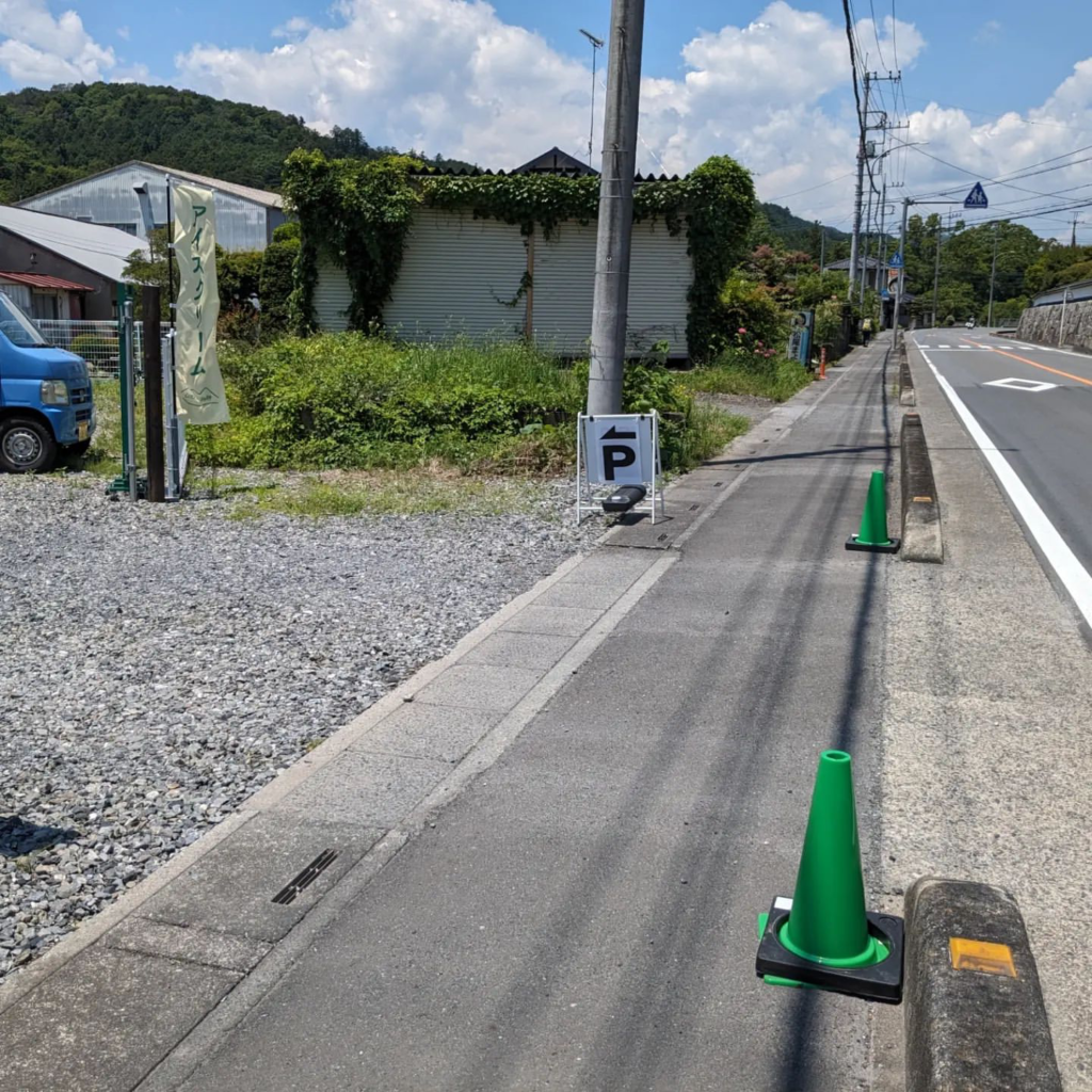 『Little Valley』の駐車場案内。緑のコーンと駐車場の看板が道路脇に設置され、アクセスのしやすさを示している。道路は片側1車線で、天気は晴れ。