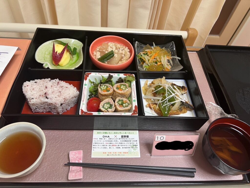 産後の入院中に提供された病院食。色とりどりの料理が一つの膳に整えられ、黒米ご飯、野菜の炒め物、鶏肉の巻き物、サラダ、スープ、デザートが並んでいる。