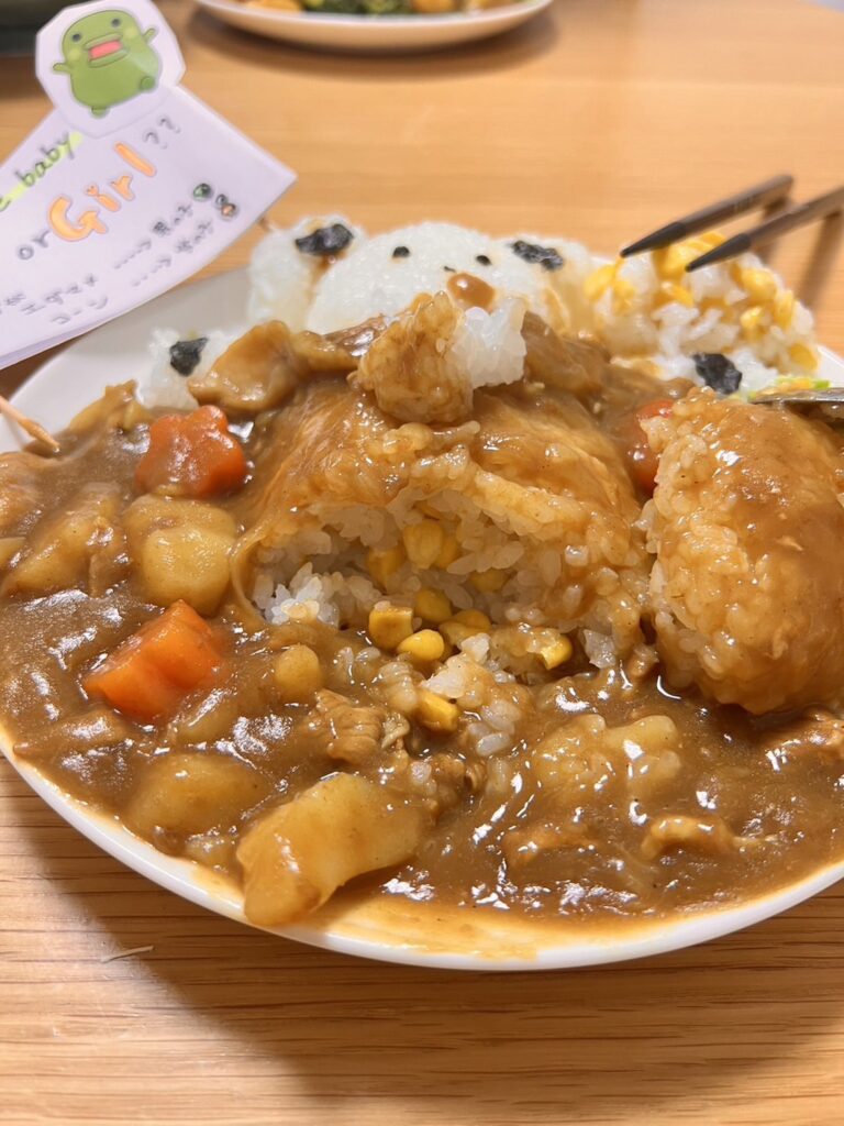 カレーライスが一部食べられ、中からコーンが見えている。ご飯のクマの顔と『Boy or Girl!?』と書かれた旗も映っている。