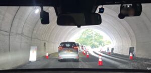 トンネル内の片側交互通行の様子。前方には車が並び、工事用コーンが並べられている。