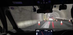 夜間または暗いトンネル内での片側交互通行。車列と反射するコーンが見える。